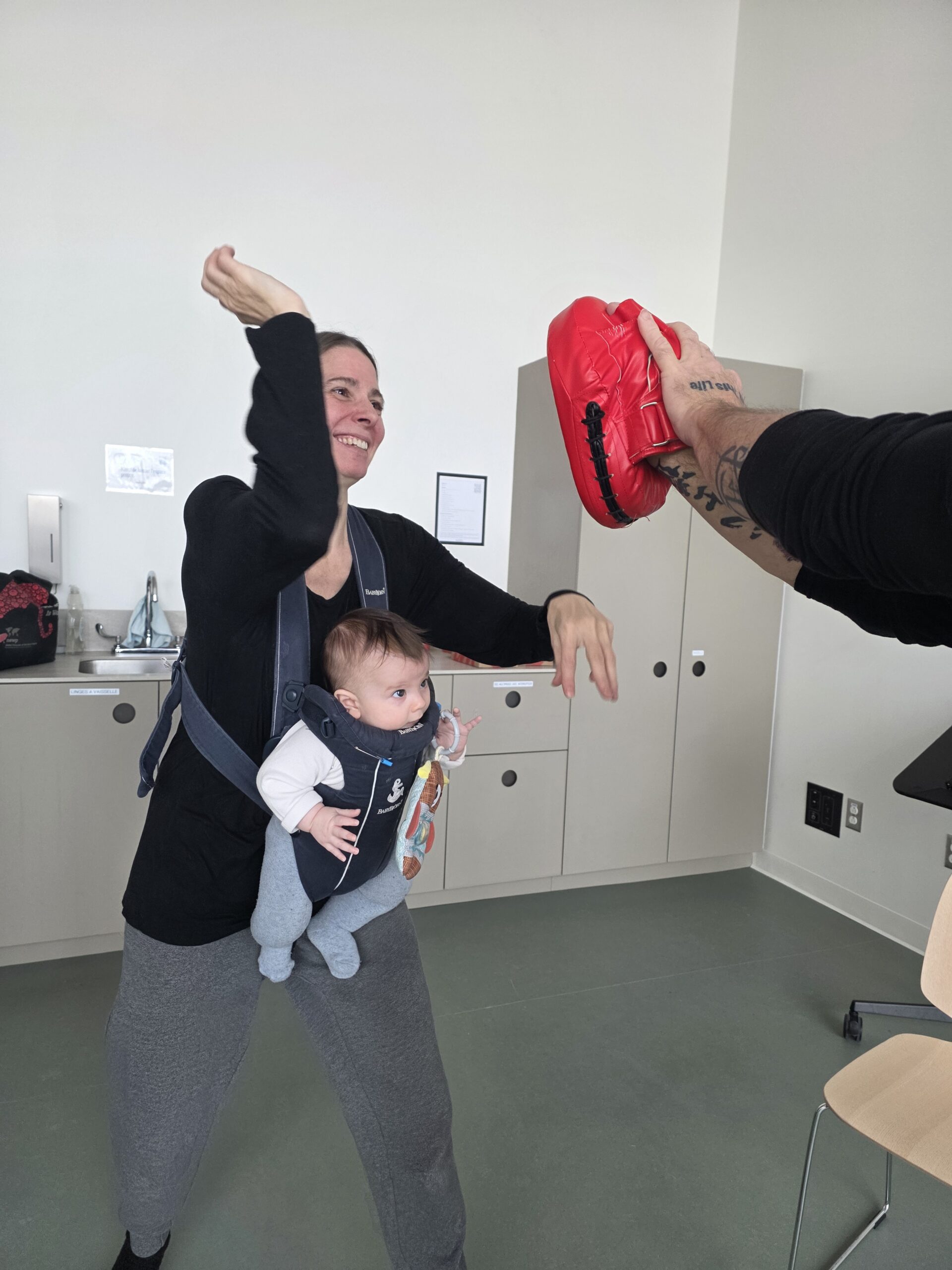 Mother learning practical self-defence skills while caring for her baby